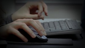 close up of hands holding a mouse and typing on a keyboard