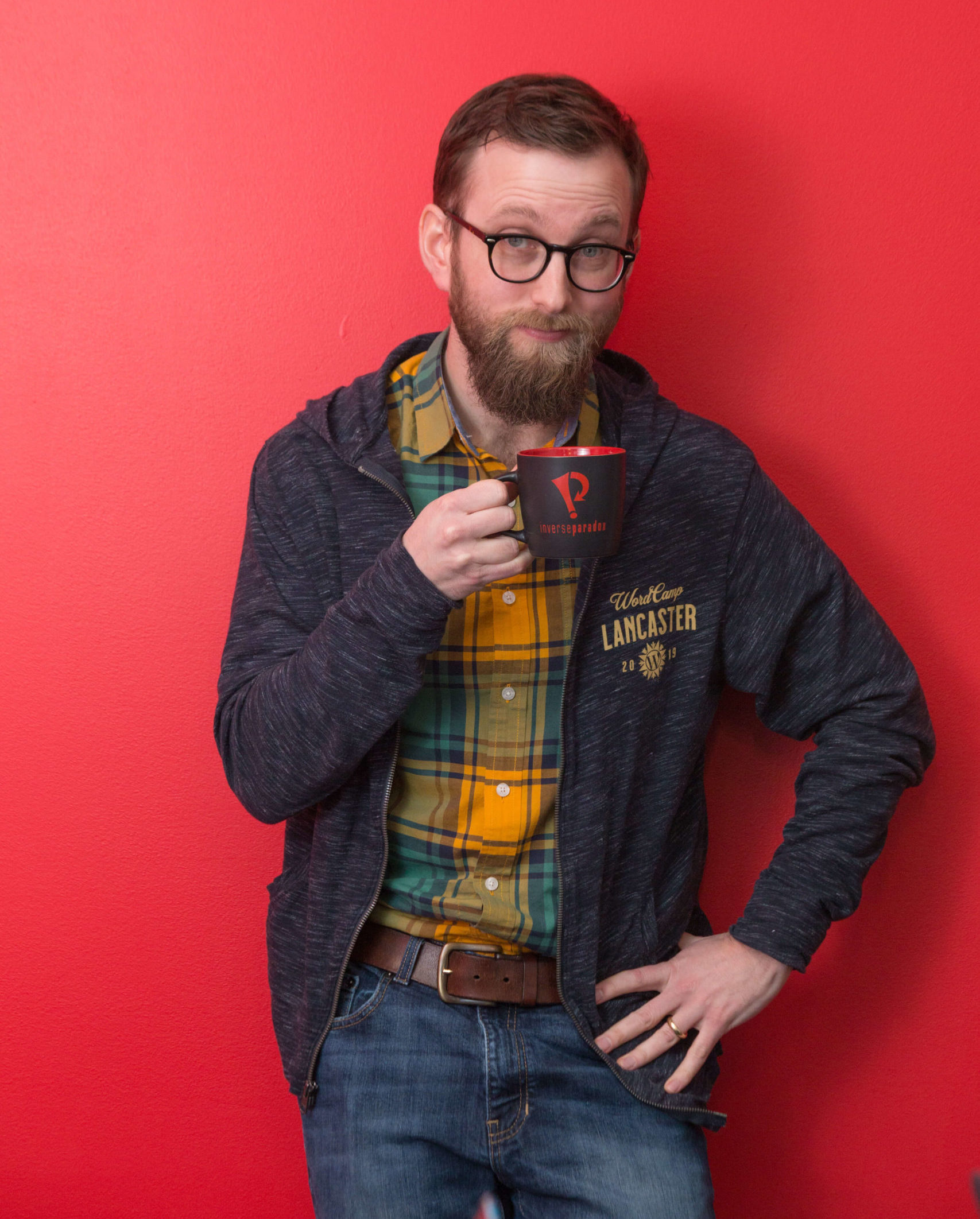 man in front of a red wall holding a coffee cup